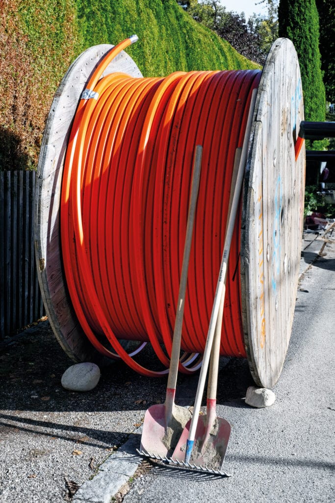Orangefarbene Glasfaserkabel auf einer großen Rolle an der Baustelle. Im Vordergrund zwei Schaufeln
