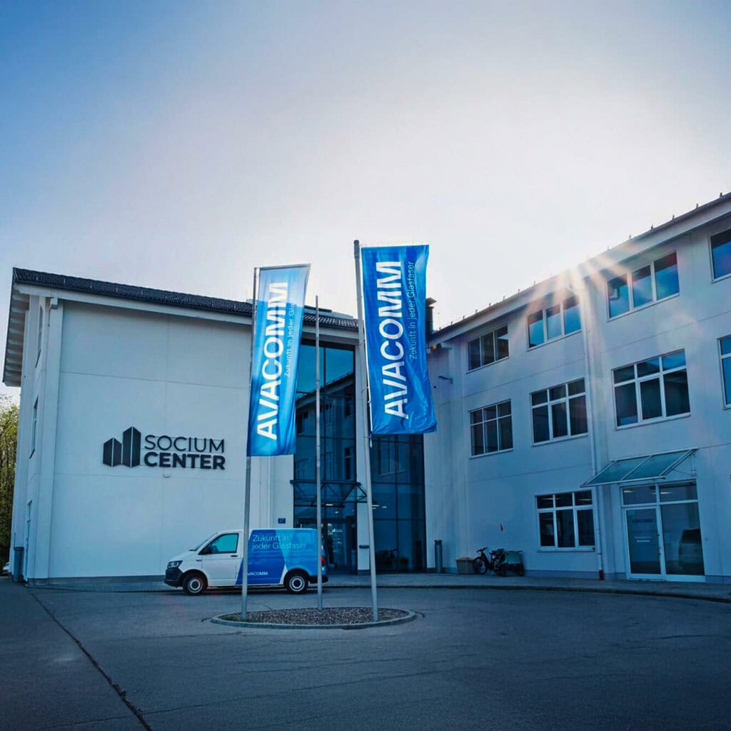 AVACOMM Firmenzentrale im Socium Center mit Glasfaser-Fahrzeug und Unternehmensfahnen – regionaler Anbieter für zukunftssichere Glasfaserlösungen.