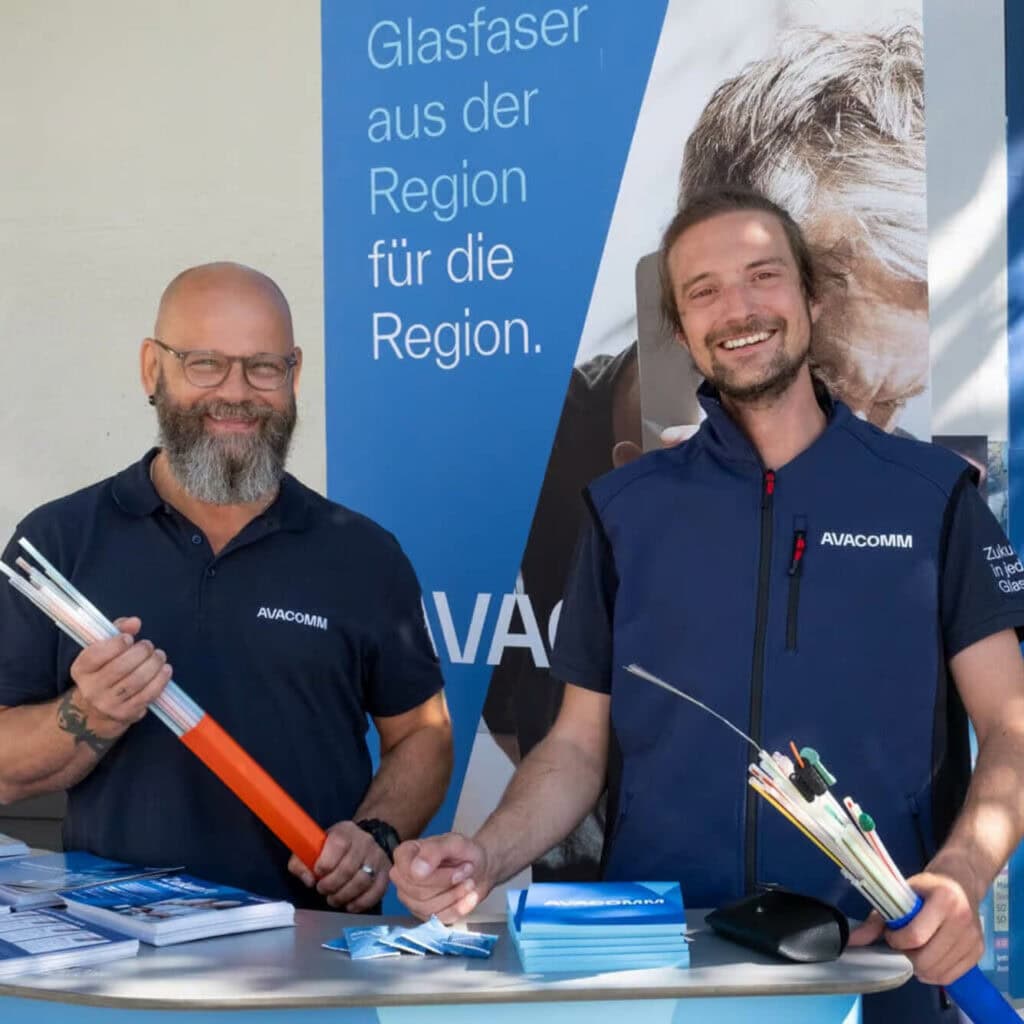 Zwei AVACOMM-Mitarbeiter präsentieren Glasfaserkabel auf einem regionalen Infostand – Glasfaser-Internet für die Region.