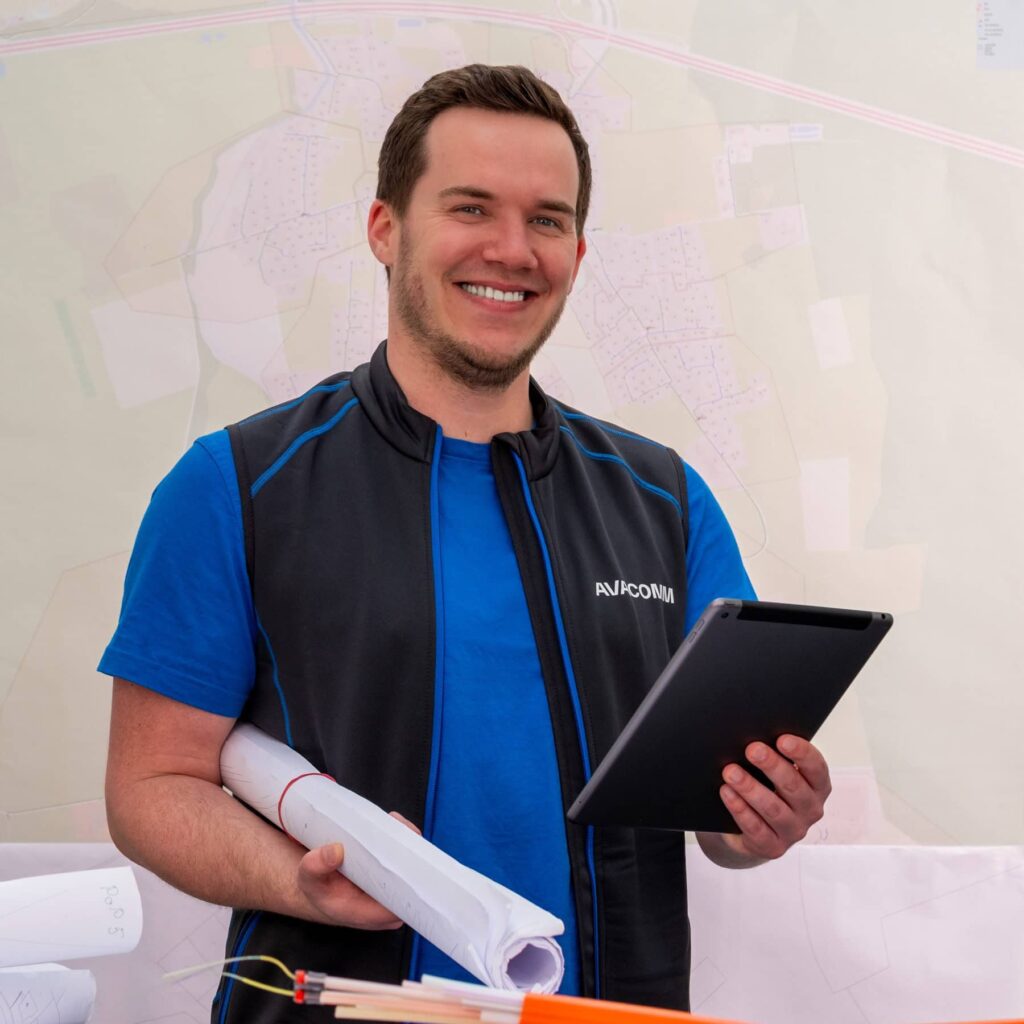 Bauleiter der AVACOMM hält ein IPad in der Hand und eine Rolle Pläne unter dem Arm