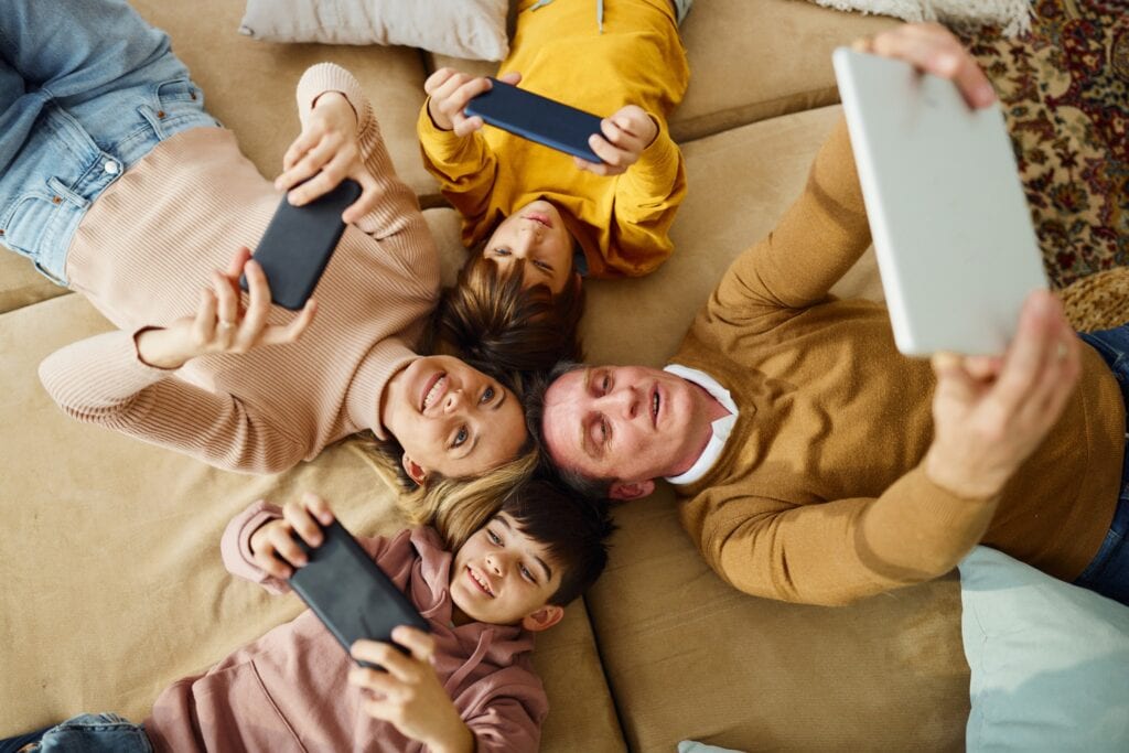 Obenansicht einer glücklichen Familie, die drahtlose Technologie zu Hause verwendet.