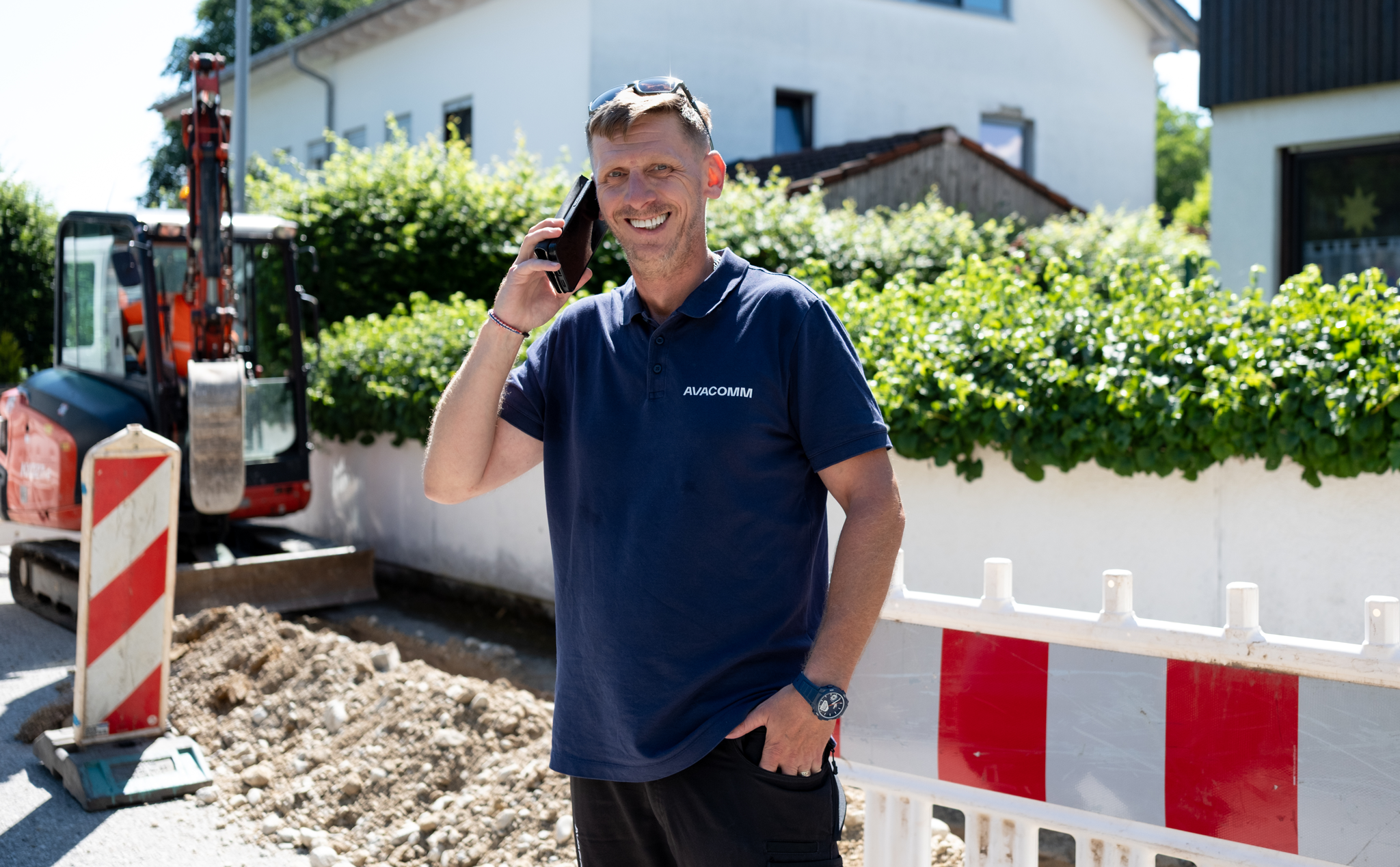 Bauleiter mit Smartphone telefonierend vor einer Baustelle zum Glasfaserausbau in Holzkirchen